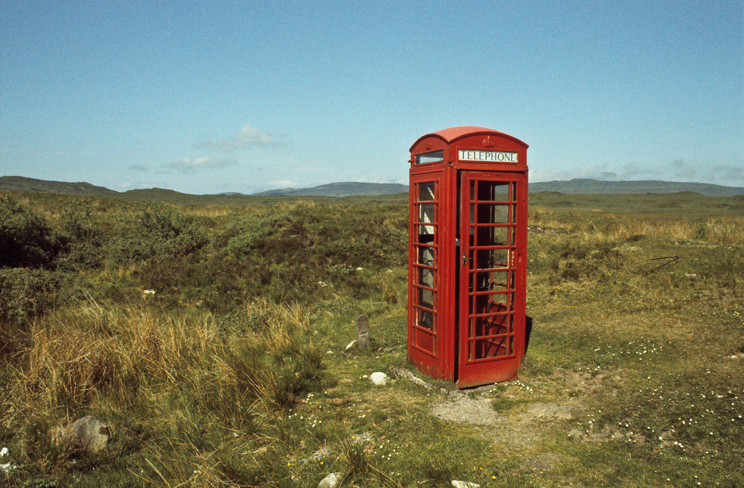 Een rode telefooncel in een verlaten landschap.