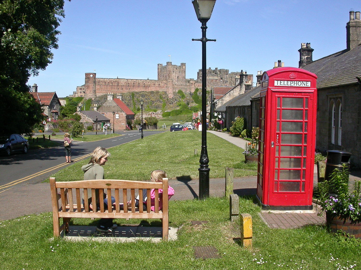 Een rode telefooncel, kinderen op een bankje en Bamburgh Castle op de achtergrond.