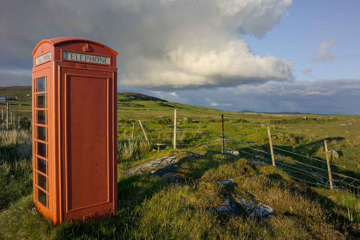 Een oude rode telefooncel met wolkenlucht op de achtertgrond.