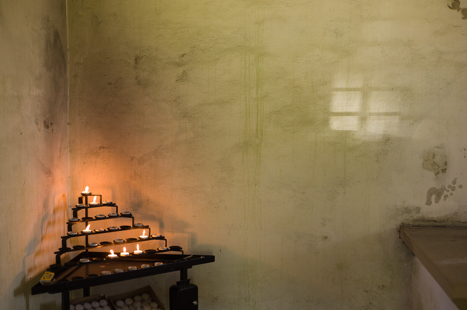 Interieur van een kerkje, wat kaarsen in de hoek en een vlek licht op de muur.
